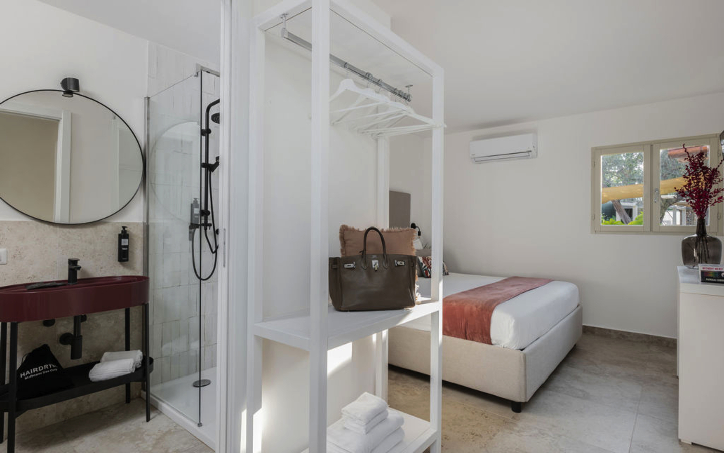 Helles Hotelzimmer mit Doppelbett und offener Dusche.