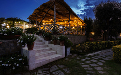 Beleuchtete Terrasse eines Restaurants am Abend mit blühenden Pflanzen und Steinweg.