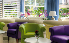 Bunte Sessel und Sofas in einem hellen Lounge-Bereich mit Fenstern und Pflanzen.