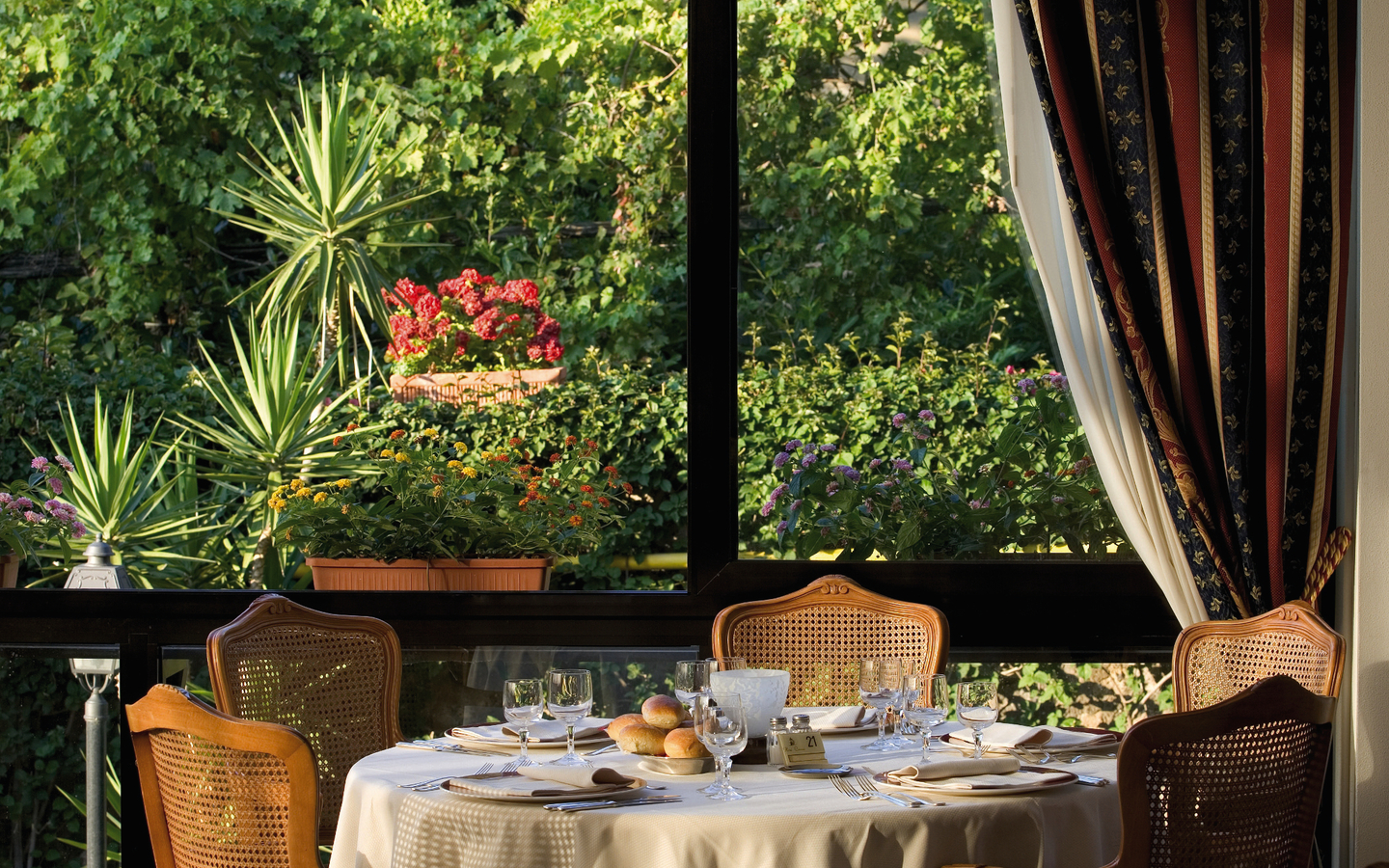 Gedeckter Tisch in einem eleganten Hotelrestaurant mit Blick auf einen grünen Garten.