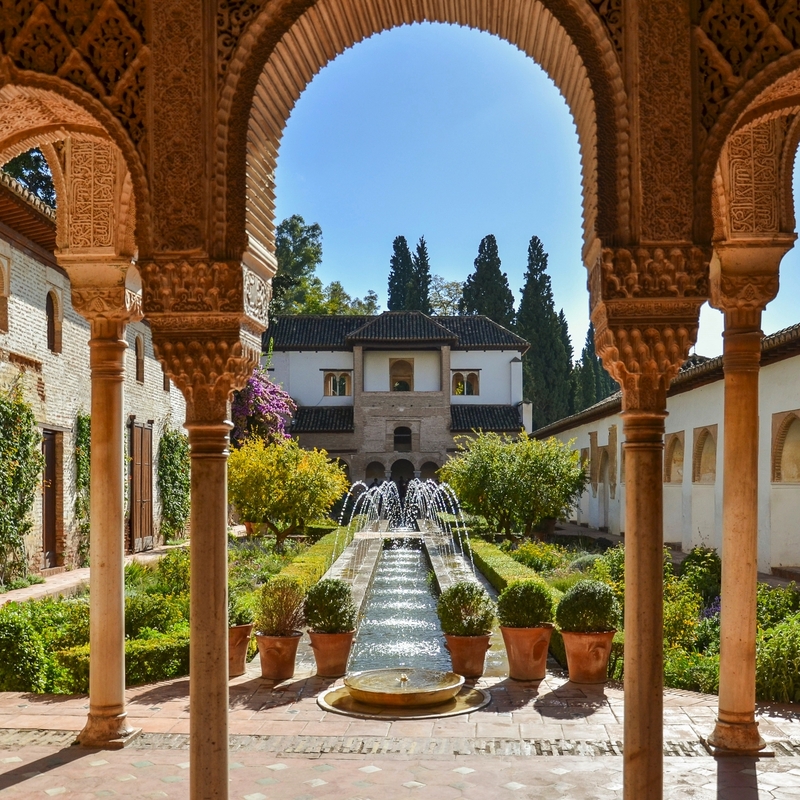 Mittelalterlicher Hof mit Arkaden und Springbrunnen im Garten.