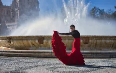 Frau in rotem Flamenco-Kleid tanzt vor einem Brunnen im Freien.