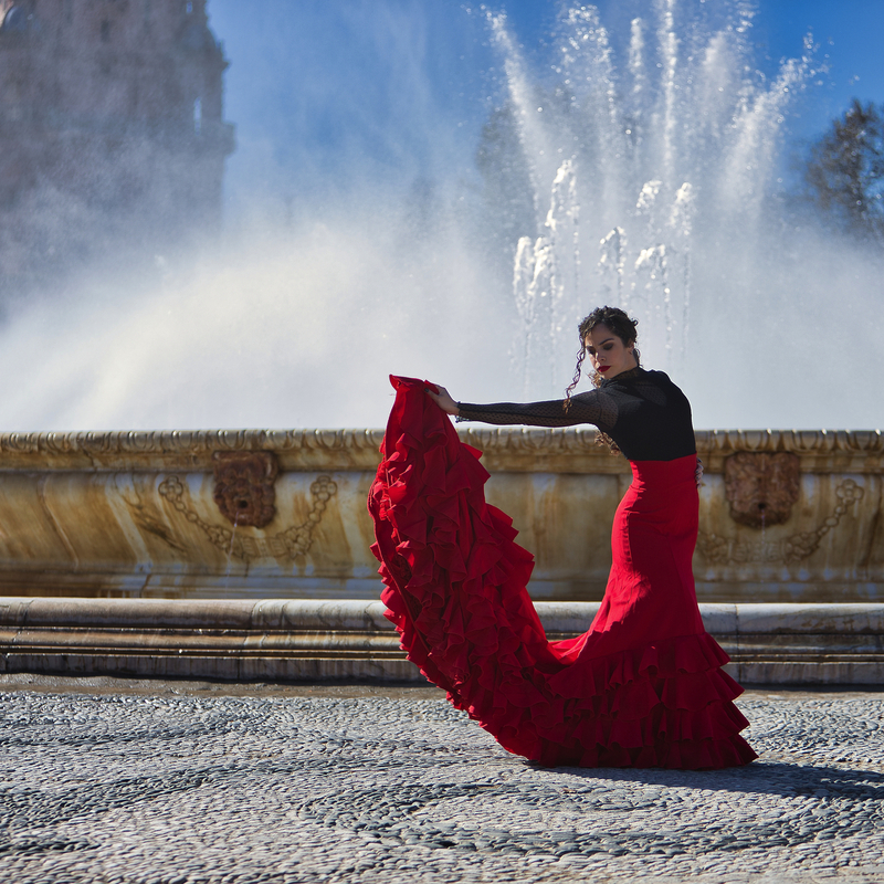 Frau in rotem Flamenco-Kleid tanzt vor einem Brunnen im Freien.