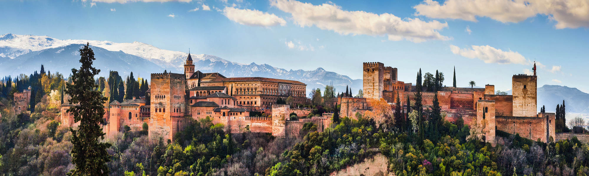 Die Alhambra in Granada vor Bergkulisse und blauem Himmel.