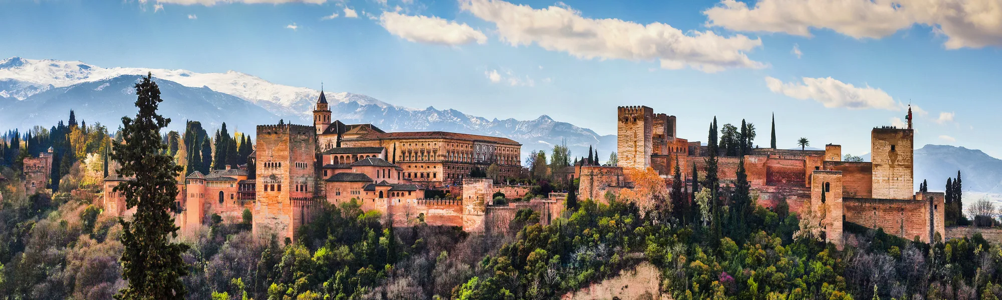 Die Alhambra in Granada vor Bergkulisse und blauem Himmel.