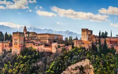 Die Alhambra in Granada vor Bergkulisse und blauem Himmel.