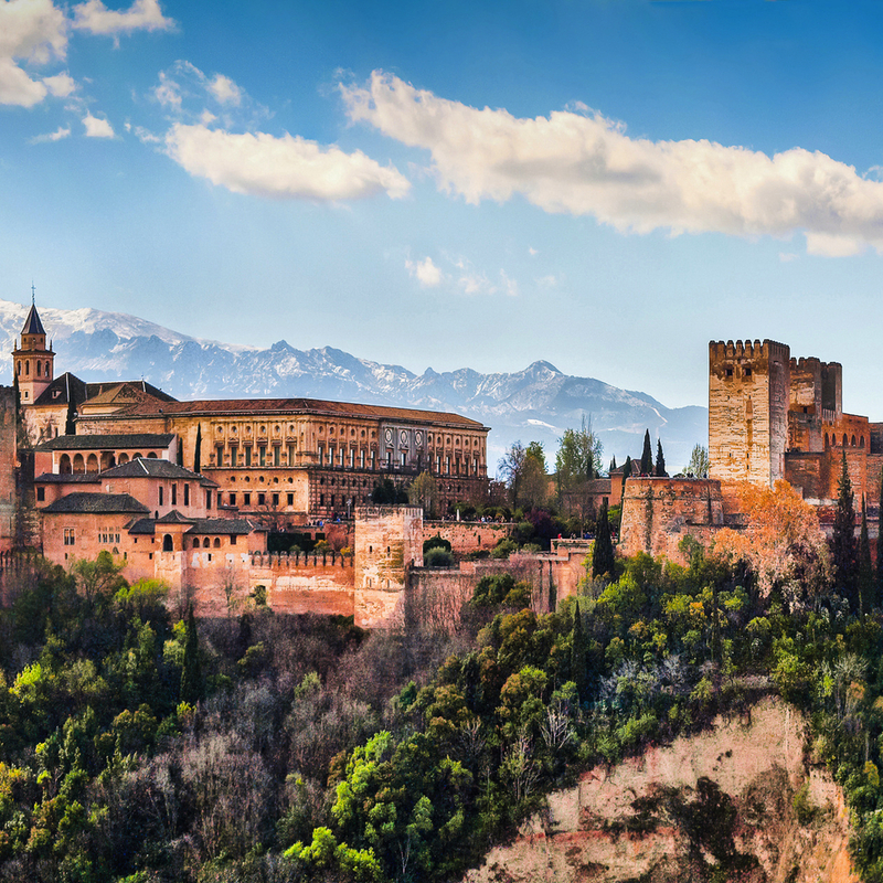 Die Alhambra in Granada vor Bergkulisse und blauem Himmel.
