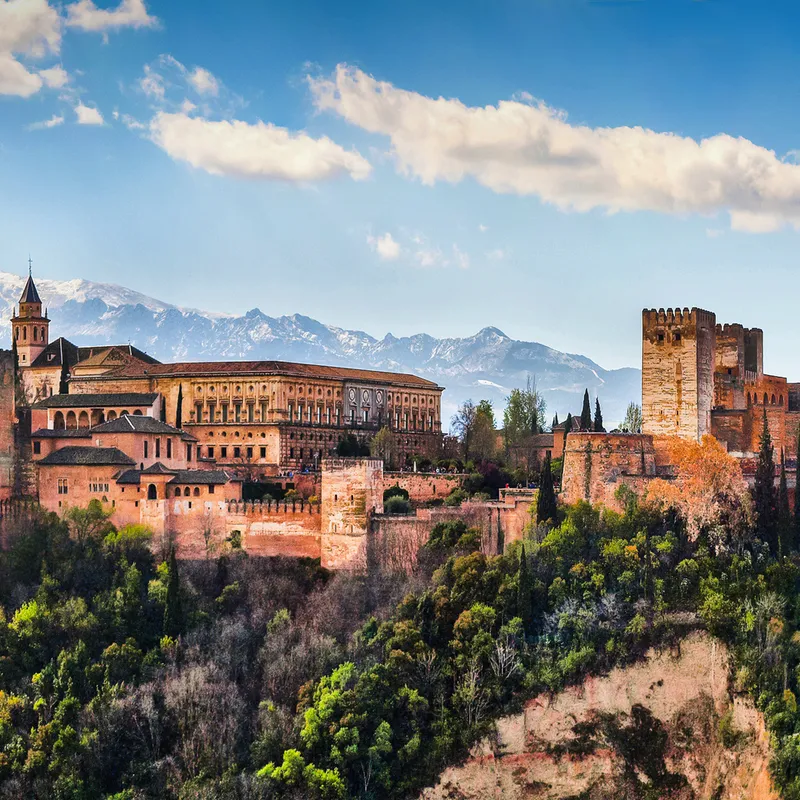 Die Alhambra in Granada vor Bergkulisse und blauem Himmel.
