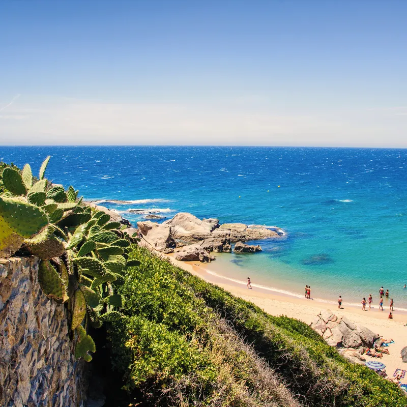 Strand mit Personen, blauem Meer und Kakteen an der Costa de la Luz, Spanien.