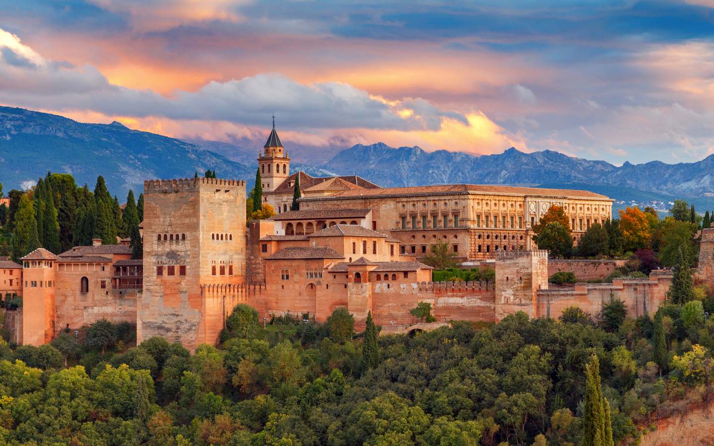 Blick auf die Alhambra in Granada bei Sonnenuntergang mit Bergen im Hintergrund.