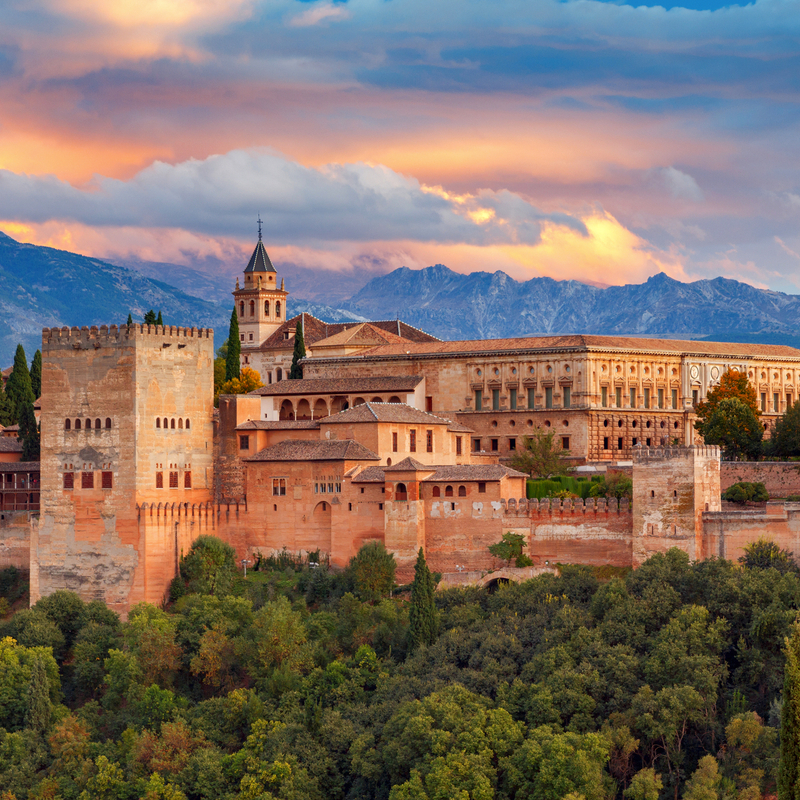 Blick auf die Alhambra in Granada bei Sonnenuntergang mit Bergen im Hintergrund.