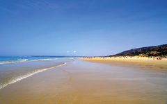 Weitläufiger Sandstrand unter klarem Himmel an der Costa de la Luz in Spanien.