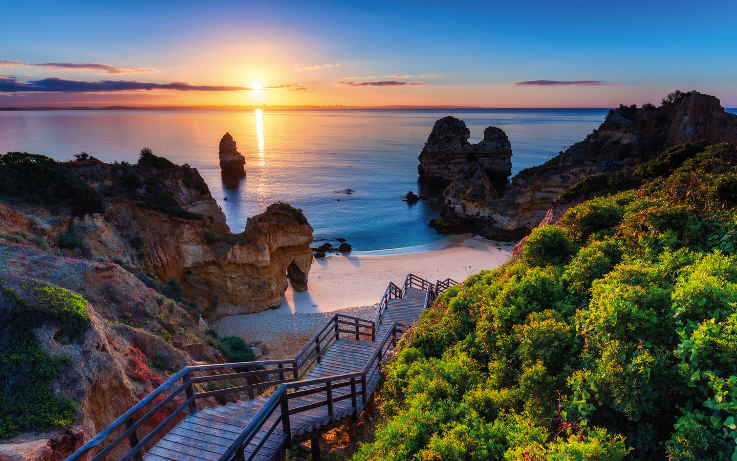 Strand mit Treppe und Felsen bei Sonnenuntergang an der Algarve, Portugal.