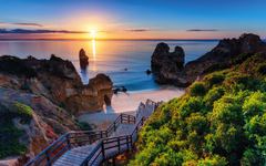 Strand mit Treppe und Felsen bei Sonnenuntergang an der Algarve, Portugal.