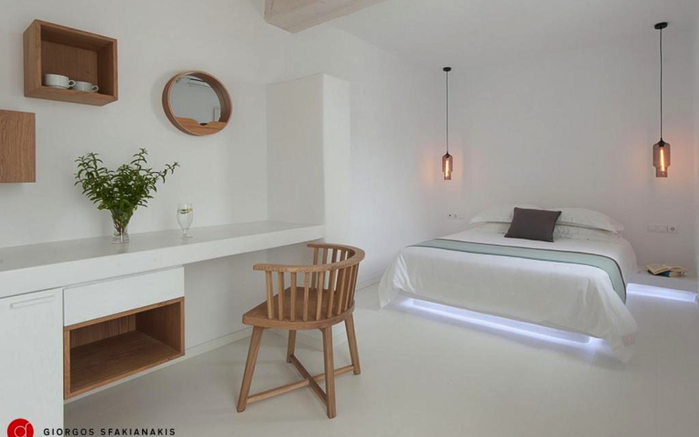 Helles Hotelzimmer auf Mykonos mit Bett, Schreibtisch und Holzstuhl.