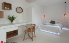 Helles Hotelzimmer auf Mykonos mit Bett, Schreibtisch und Holzstuhl.