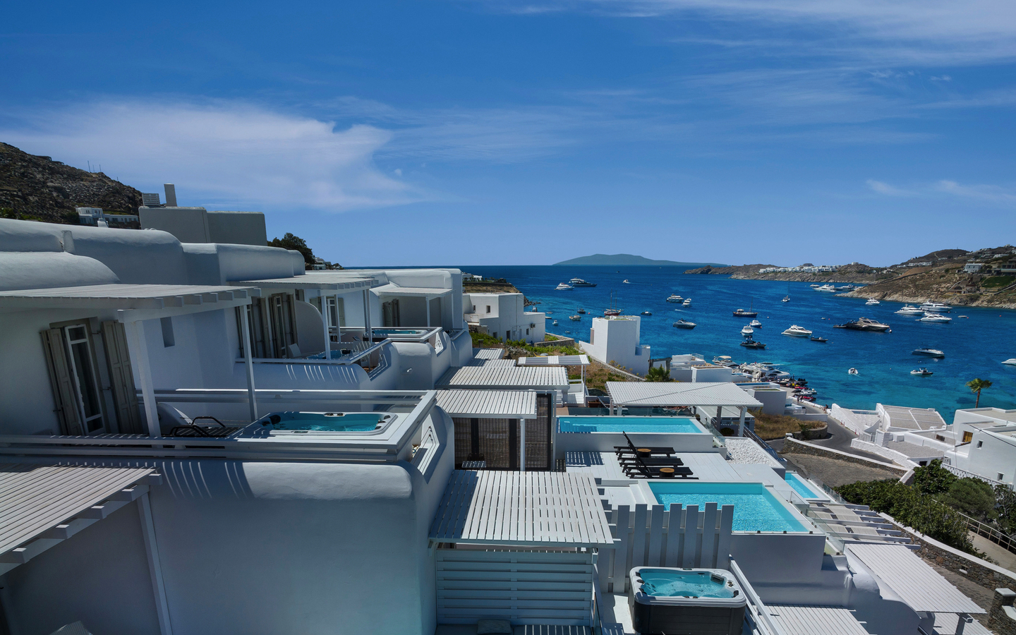 Hotel mit weißen Gebäuden und Pools, Blick aufs Meer und Boote, Mykonos, Griechenland.