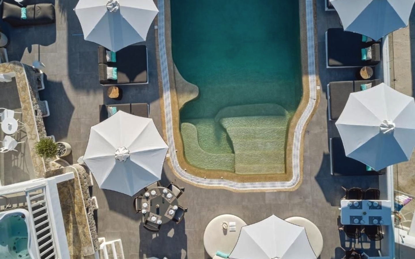 Poolbereich eines Hotels auf Mykonos mit Liegestühlen und Sonnenschirmen aus der Vogelperspektive.
