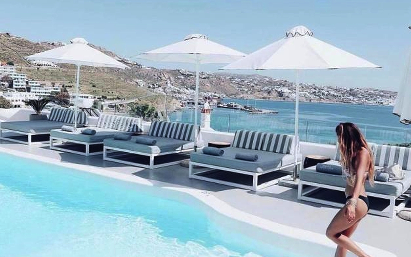 Frau am Pool mit Blick aufs Meer, Sonnenschirme und Liegestühle im Hintergrund.