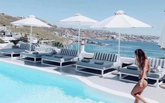Frau am Pool mit Blick aufs Meer, Sonnenschirme und Liegestühle im Hintergrund.