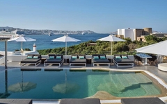 Pool mit Liegen und Sonnenschirmen, Blick auf das Meer und Mykonos im Hintergrund.