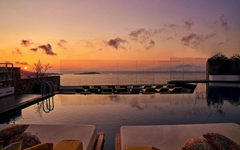 Pool mit Liegen und Blick auf das Meer bei Sonnenuntergang im Myconian Korali Hotel.
