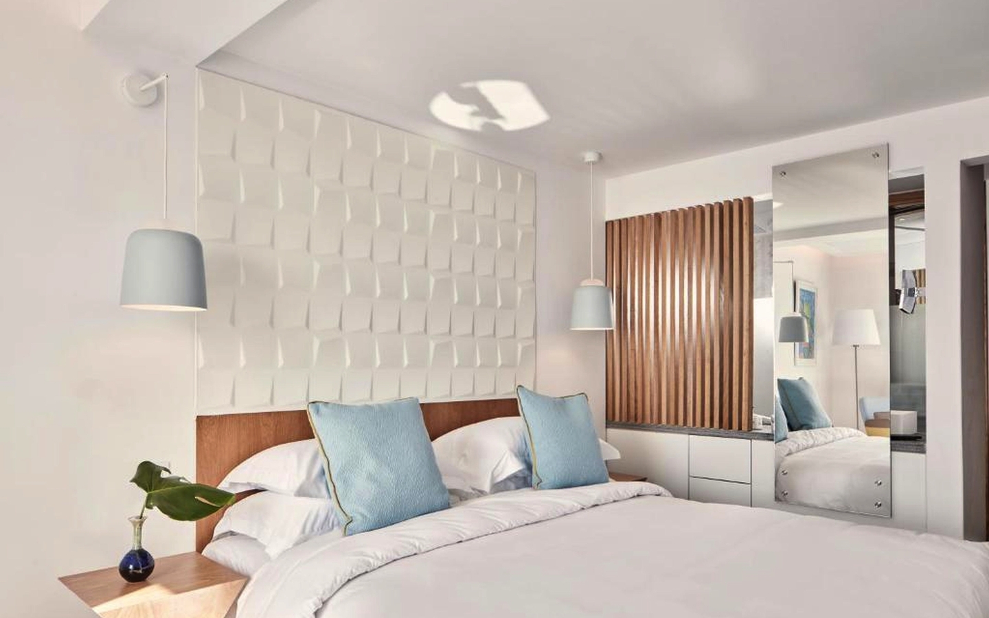Helles Hotelzimmer mit Doppelbett, blauen Kissen und modernem Dekor.
