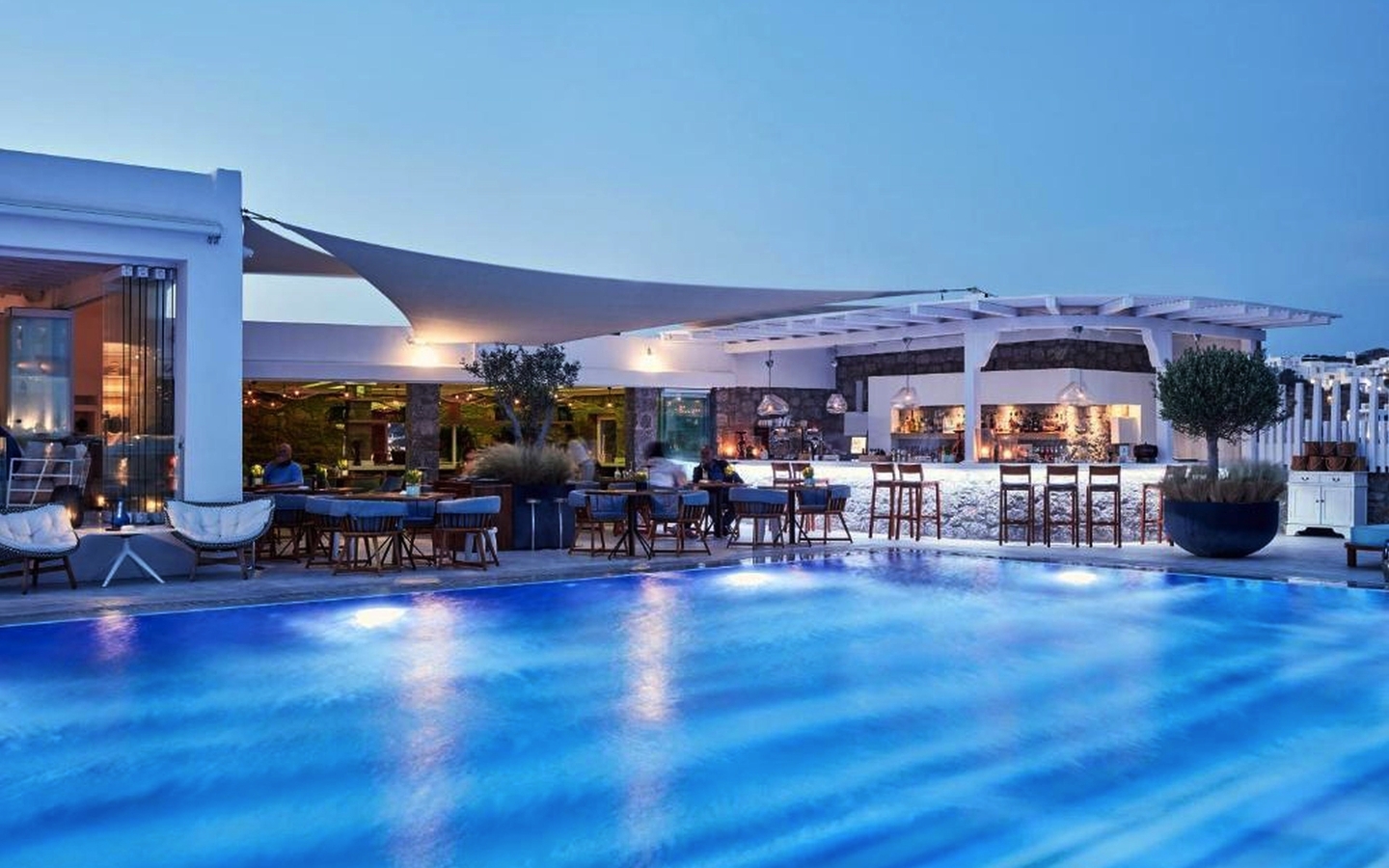 Pool mit Terrasse und Bar im Hotel Myconian Korali auf Mykonos bei Abenddämmerung.