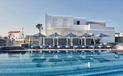 Poollandschaft eines Hotels auf Mykonos mit weißer Gebäudefassade im Hintergrund.