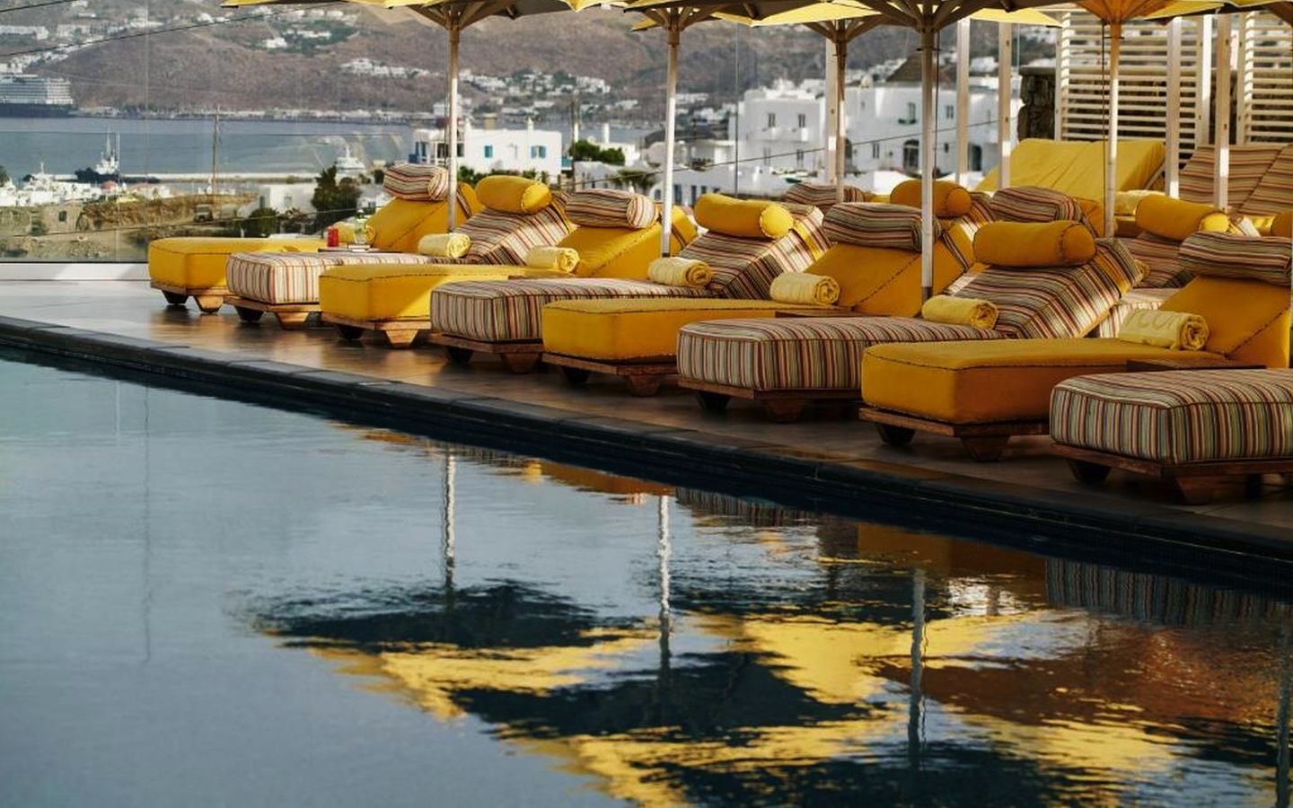 Gelbe Liegestühle und Sonnenschirme am Pool, Blick auf Mykonos.