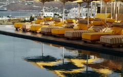 Gelbe Liegestühle und Sonnenschirme am Pool, Blick auf Mykonos.