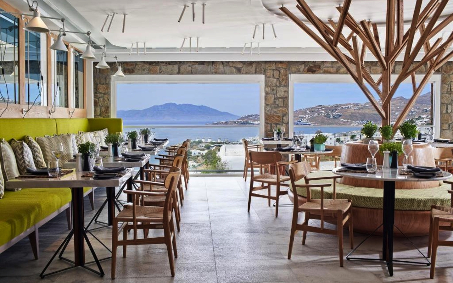 Modernes Restaurant mit Meerblick, Holzmöbeln und grüner Polsterbank in Mykonos.