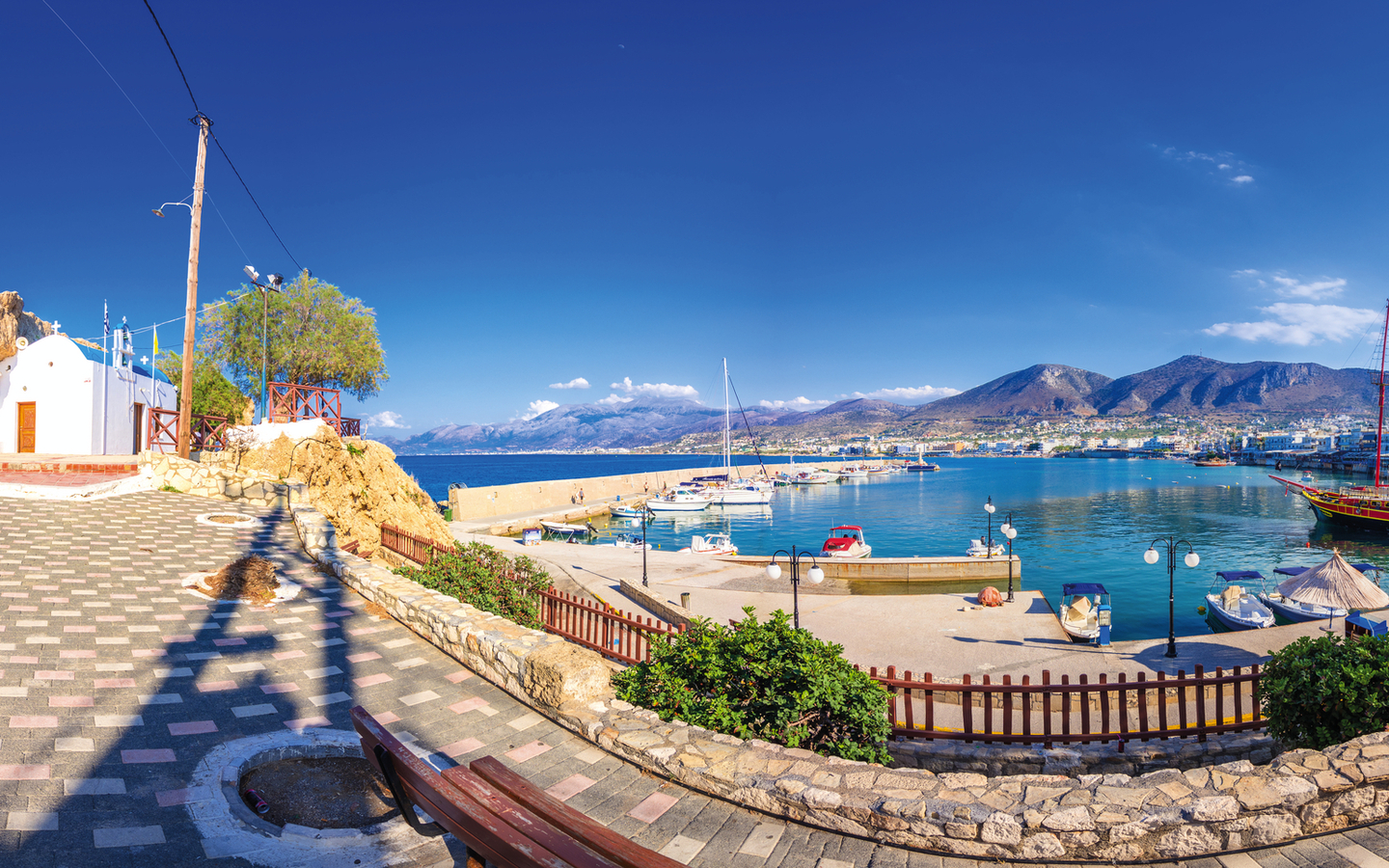 Hafen von Chersonissos auf Kreta mit Booten und hügeliger Landschaft im Hintergrund.