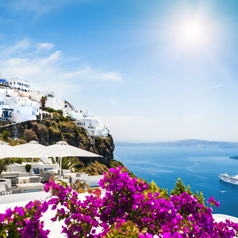 Küstenstadt mit weißen Häusern und Bougainvillea, Blick aufs Meer und Kreuzfahrtschiff.