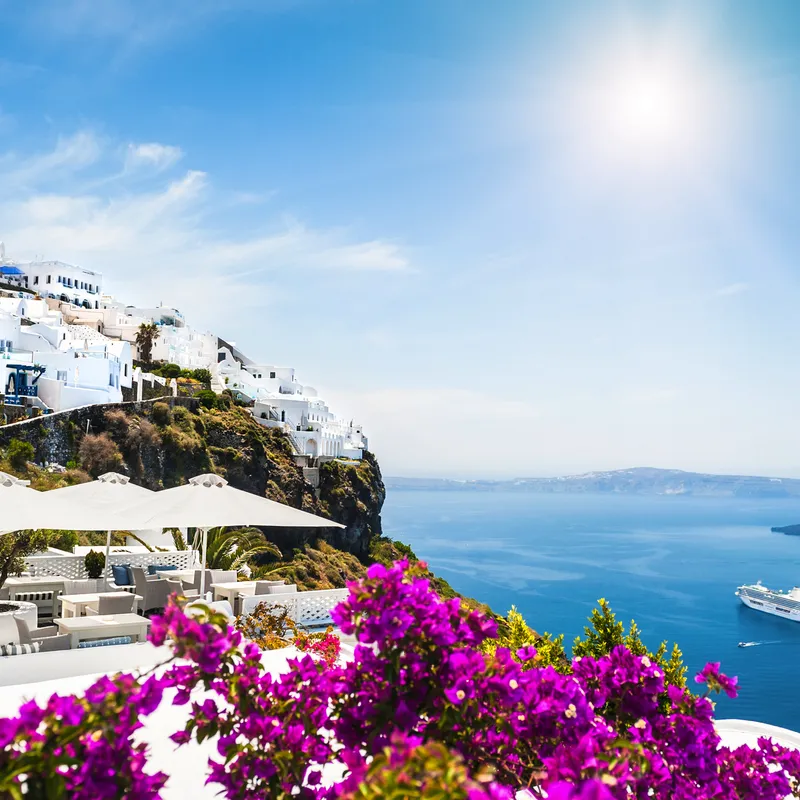 Küstenstadt mit weißen Häusern und Bougainvillea, Blick aufs Meer und Kreuzfahrtschiff.