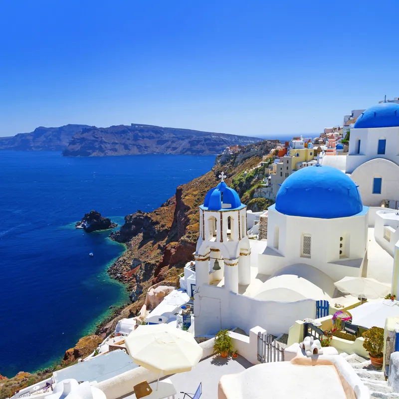 Weiße Gebäude mit blauen Kuppeln auf Santorini, Meer im Hintergrund.