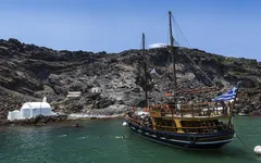 Traditionelles Schiff vor vulkanischer Küste Santorins, Griechenland.