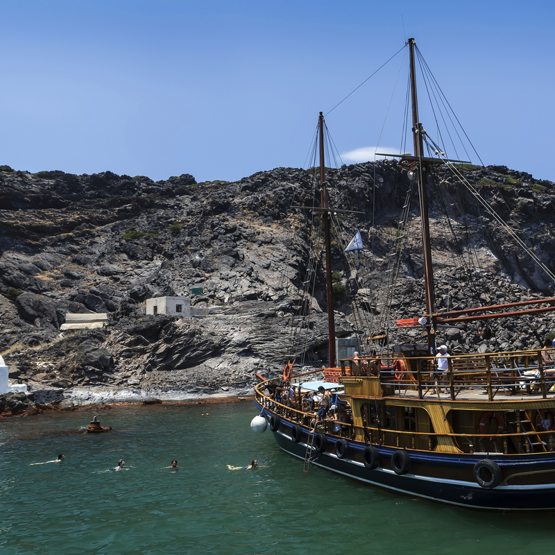 Traditionelles Schiff vor vulkanischer Küste Santorins, Griechenland.