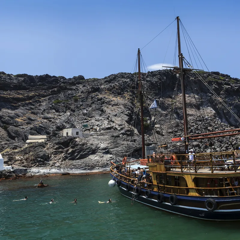 Traditionelles Schiff vor vulkanischer Küste Santorins, Griechenland.