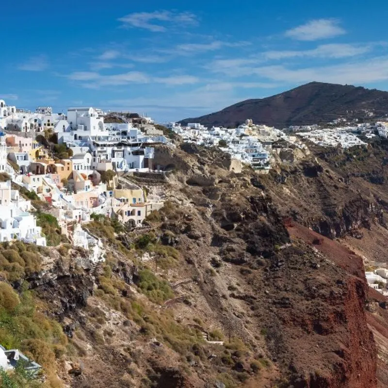 Küstenstadt auf Santorin mit weiß-blauen Gebäuden und Blick aufs Meer.