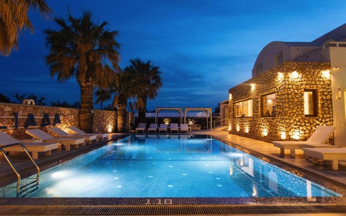 Poolbereich des Iliada Odysseas Resorts bei Abenddämmerung auf Santorin.