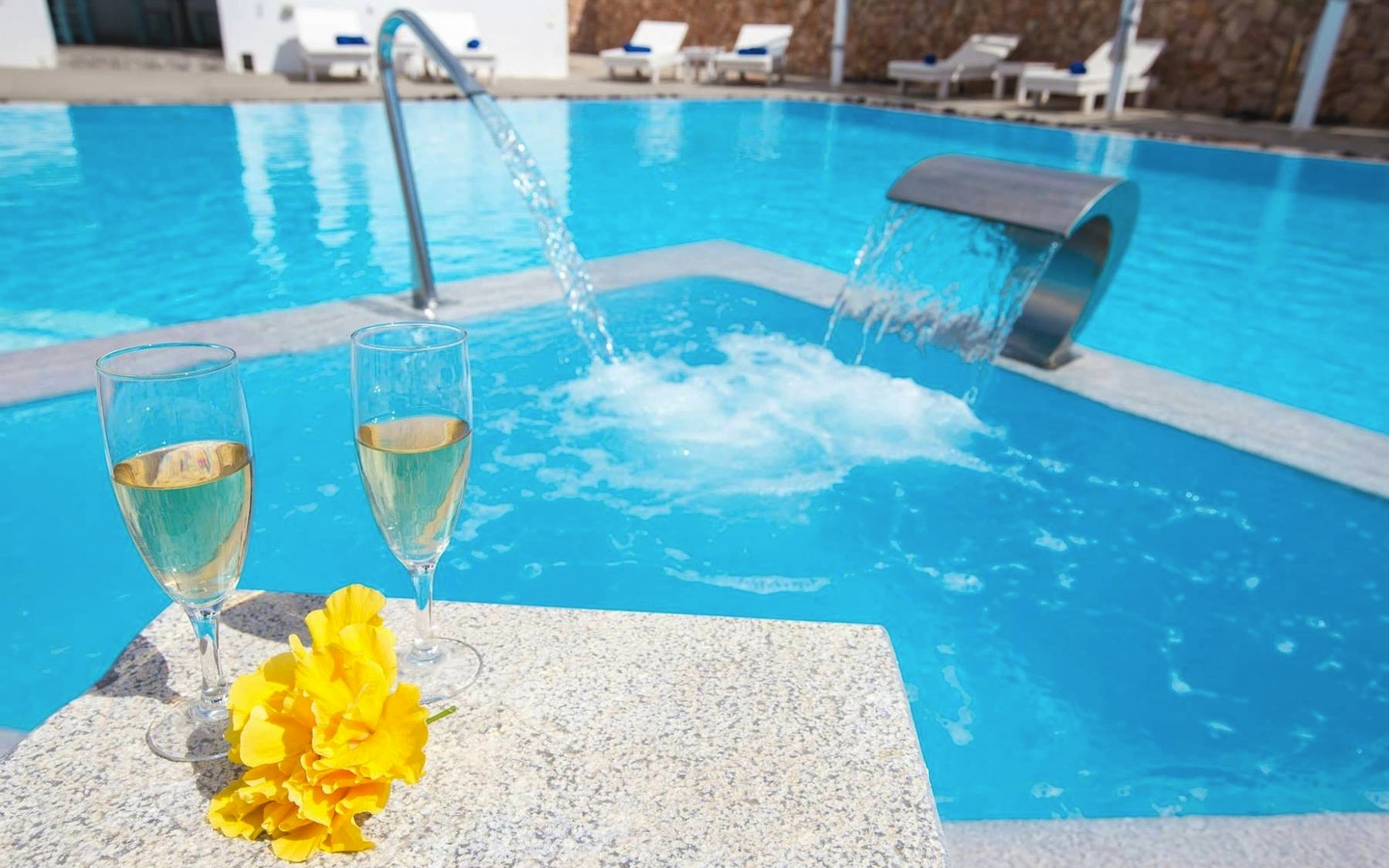Pool mit Wasserfall, zwei Sektgläsern und gelben Blumen im Iliada Odysseas Resort.