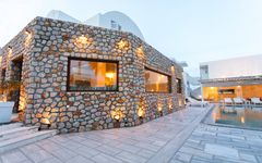 Steinhaus am Iliada Odysseas Resort mit Pool auf Santorin bei Sonnenuntergang.