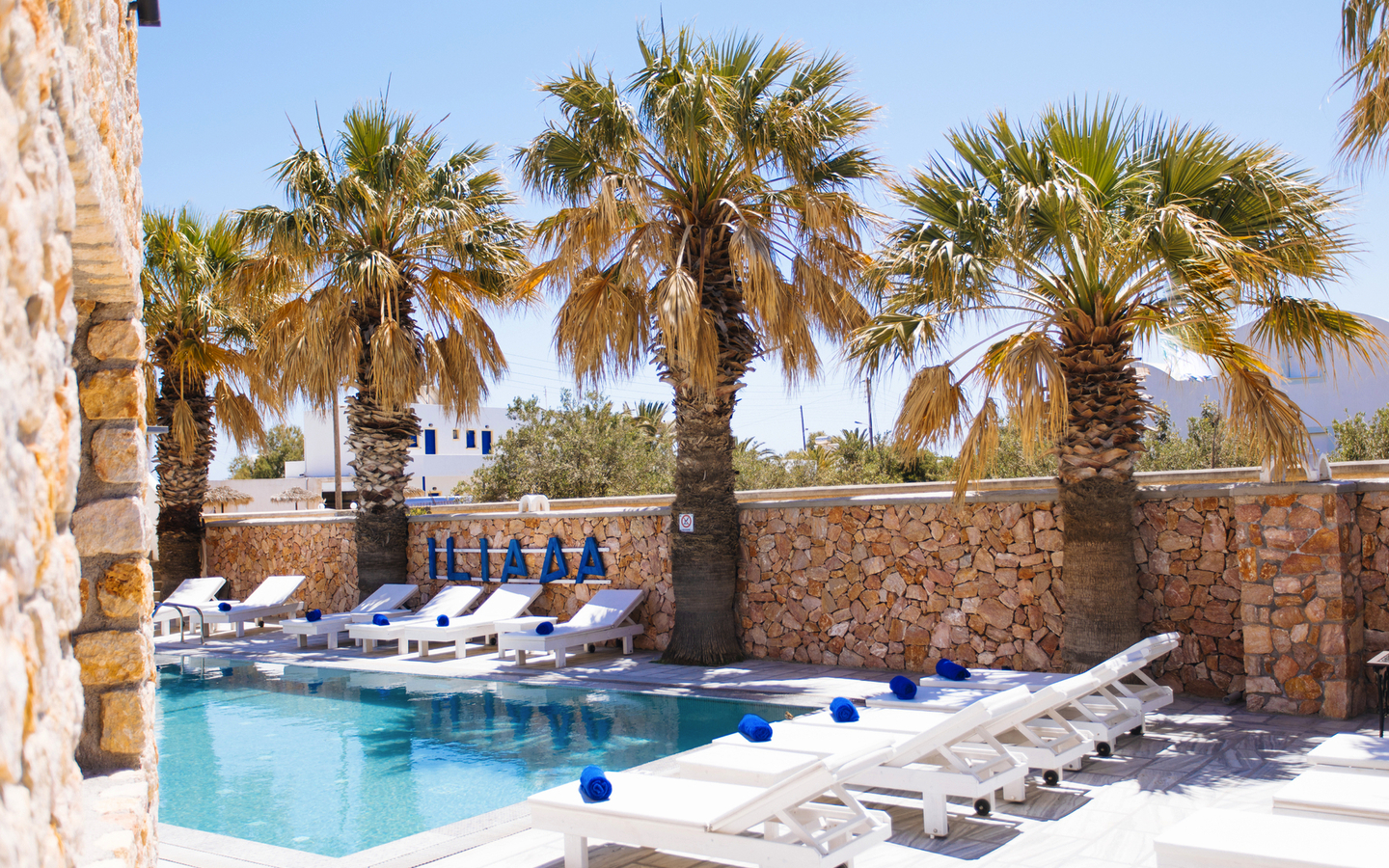 Poolbereich mit Liegestühlen und Palmen im Iliada Odysseas Resort, Santorin.
