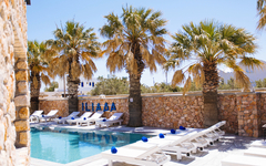 Poolbereich mit Liegestühlen und Palmen im Iliada Odysseas Resort, Santorin.