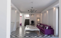 Helle Lounge mit lila Sofa, weißen Wänden und Schachbrettboden, Kronleuchter oben.