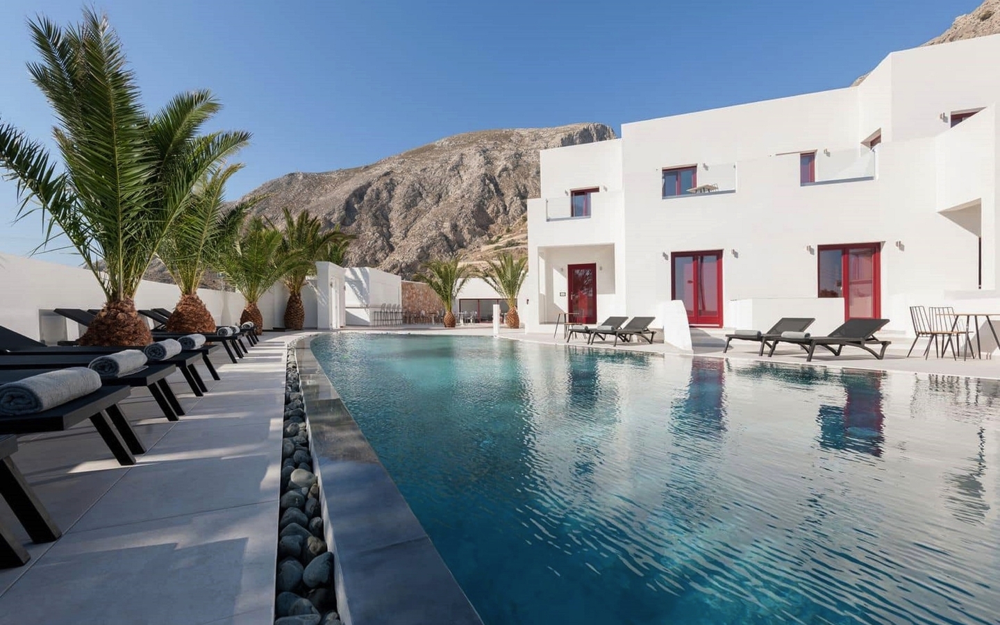 Hotel mit Pool, Palmen und Berge im Hintergrund in Santorin, Griechenland.