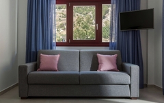 Graues Sofa mit rosa Kissen vor Fenster, blaue Vorhänge und Fernseher.