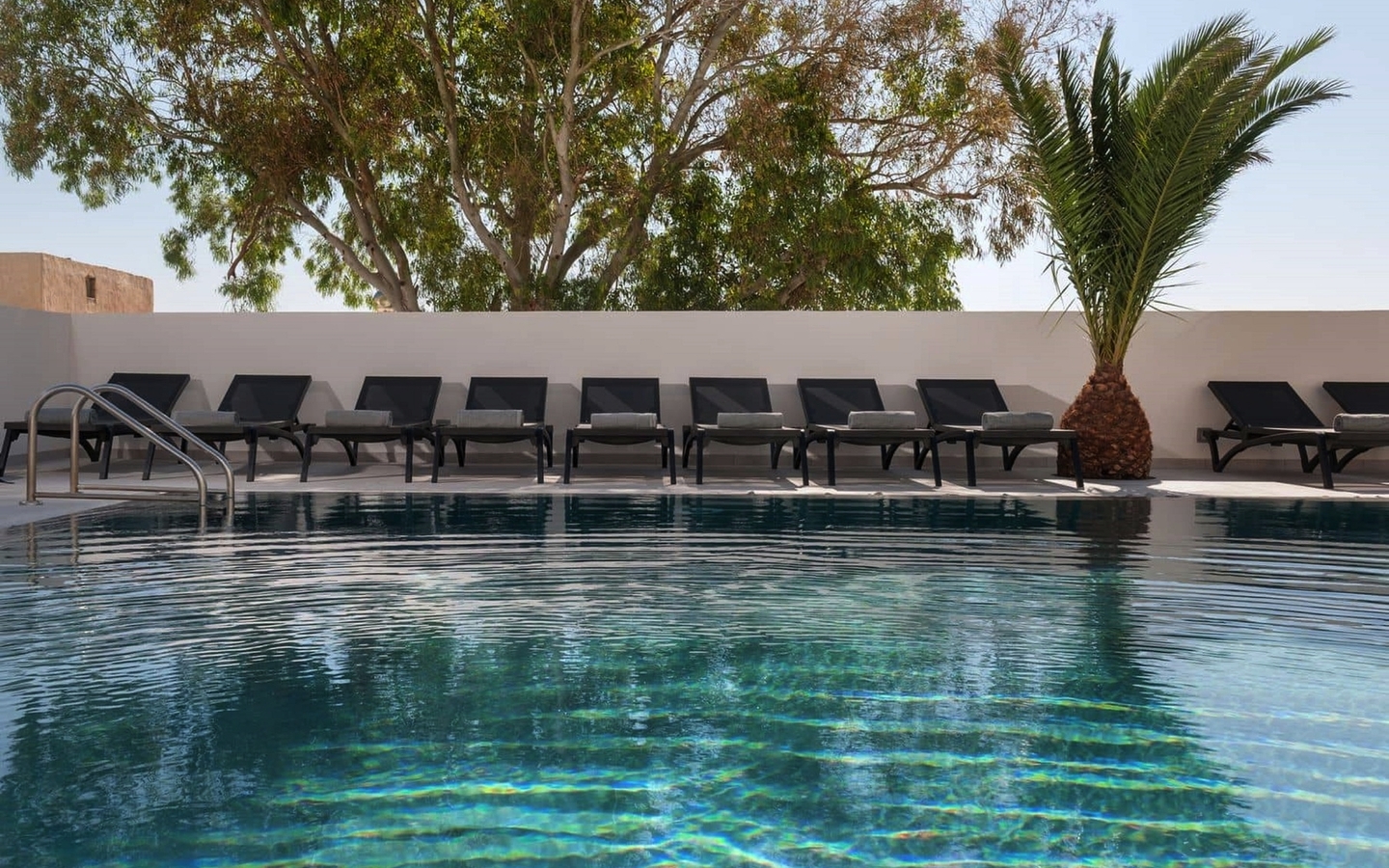 Pool mit Liegestühlen und Pflanzen im Hintergrund bei Mar n Mar Crown Hotel, Santorin.
