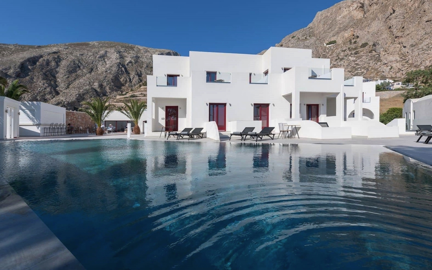 Weißes Hotelgebäude mit Pool und Bergkulisse auf Santorin, Griechenland.